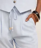Pantalón celeste de corte recto, confeccionado en tejido de lino y viscosa. Presenta cintura elástica con lazo ajustable, bolsillos laterales y pliegues frontales.