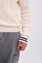Buzo de tejido de punto con diseño de ochos, color crudo, con cuello redondo, puños y dobladillo acanalados con líneas azul marino y blancas.