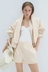 Short de mezcla de algodón y lino color beige, con pinzas delanteras, raya marcada al frente y ajuste con hebillas metálicas en los laterales.