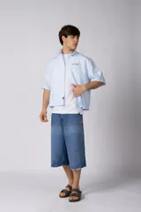Camisa de manga corta de popelina rayada, con calce boxy y bordado sutil en el pecho. Presenta cierre frontal con botones y diseño abierto.