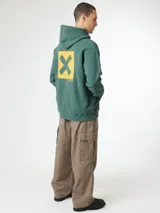 Hoodie azul marino con capucha, bolsillo tipo canguro y gran estampado cuadrado en la espalda con una letra X negra sobre fondo beige.