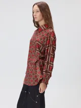 Camisa de seda con cuello camisero, manga larga y bolsillo frontal. Presenta un diseño estampado geométrico de cuadrados en tonos marrones y azul oscuro.