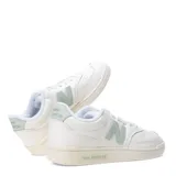 Championes urbanos New Balance, modelo Pop N Pack Leather, de color blanco con detalles en verde pastel en el logo lateral y la suela. Presentan una silueta clásica de corte bajo con perforaciones en la puntera y cierre de cordones.
