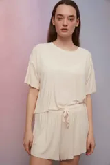 Pijama confeccionado en suave tela punto rib de color arena, compuesto por una remera de manga corta con cuello redondo y un short con cintura elástica ajustable mediante cordón.