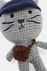 Llavero con dije tejido a crochet con forma de gato gris, que lleva una gorra azul marino y una pequeña bandolera marrón. Incluye un mosquetón metálico dorado para su sujeción.