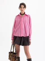 Camisa blanca de poplin con fit holgado, cuello con broche metálico y mangas largas con puños abotonados. Presenta un patrón de rayas verticales formadas por bordados de boquitas.