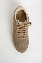 Zapatilla deportiva de gamuza color visón, con cordones a tono y suela de goma marrón. Presenta un diseño retro de running con el nombre de la marca grabado en dorado en el lateral.