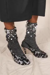 Zapato de tacón destalonado con abalorios y lentejuelas en tonos negros y plateados, escote redondo, punta redonda y tacón fino alto.