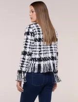 Chaqueta de tweed en blanco y negro con patrón de cuadros, escote redondo, bolsillos frontales con botones metálicos y flecos decorativos en los bordes y puños.