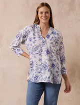 Blusa estampada con flores azules sobre fondo blanco, marca Floral & Ivy. Tiene cuello a la base con escote en V y aplique de botones. Las mangas son tres cuartos con puño y botón. Presenta tajos en las costuras laterales.