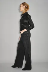 Jean de corte wide leg en color negro, con diseño de paneles laterales que crean un efecto de abertura o contraste en el bajo. Posee tiro medio y cierre clásico con botón y cremallera.