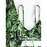 Conjunto de traje de baño de tres piezas con estampado de hojas tropicales en tonos blanco y negro. Incluye un top tipo tankini con cordón ajustable en el centro, un short de tiro alto y una camisa abierta de manga larga tipo salida de baño.