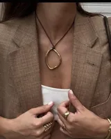 Collar con dije colgante de forma orgánica e irregular, acabado dorado, suspendido de un cordón negro de algodón natural.