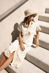 Vestido camisero de lino color lila con bordados rojos en contraste. Presenta un diseño de largo midi con cuello camisero, cierre frontal de botones y mangas cortas. Los detalles bordados recorren la botonadura, los puños y el ruedo de la prenda.