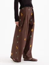 Pantalón de silueta holgada, color marrón, confeccionado en twill de algodón con estampa de flores amarillas y moras. Cuenta con bolsillos laterales y cierre frontal con botón y gancho.