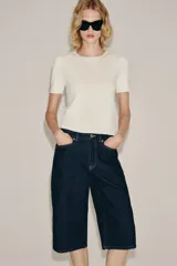 Bermuda de denim azul oscuro de tiro medio y corte recto, perteneciente a la ZARA Woman Collection. Cuenta con diseño de cinco bolsillos, trabillas para cinto y cierre frontal con cremallera y botón metálico.