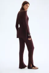 Pantalón de tiro alto, color marrón oscuro, confeccionado en tejido de punto acanalado. Presenta elástico oculto en la cintura y bajos acampanados con abertura lateral.