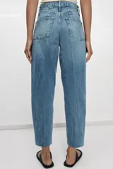 Jeans de tiro alto con corte tapered y largo al tobillo. Presenta cinco bolsillos, trabillas en la cintura, cierre frontal con cremallera y botón, y detalle de raya planchada en el delantero.