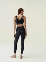 Top deportivo negro de sujeción media-alta, con escote en V y tirantes dobles en los hombros. Presenta paneles centrales con textura acanalada y una banda ancha inferior.