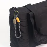 Cartera tipo tote color negro con diseño acolchado de ondas y doble asa de mano. Incluye un mosquetón decorativo con cordón trenzado en el lateral.