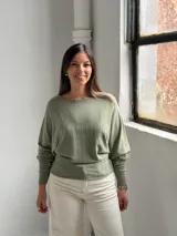 Sweater de punto color verde oliva, con cuello bote y mangas murciélago. Presenta un diseño de textura acanalada vertical en el frente y puños ajustados.