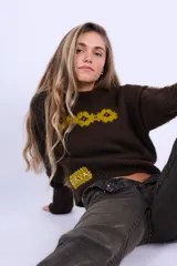Sweater de lana merino color chocolate, tejido a dos agujas con diseño de flores bordadas en color amarillo en el pecho y parche decorativo con texto en la parte inferior.