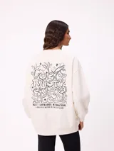 Sweater color crema de corte holgado, con cuello redondo y manga larga. Presenta un estampado gráfico en la espalda con el texto "RUSTY SURFBOARDS INTERNATIONAL A BREATH OF NATURE IN THE CITY'S CORE" rodeado de motivos florales y abstractos en color negro.
