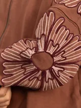 Campera de jogging negra con cierre frontal, cuello con detalle de volados y bordados florales en las mangas. Presenta un corte holgado y puños elásticos.