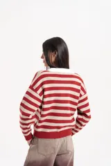 Buzo de punto con diseño a rayas horizontales en tonos marrón y beige. Presenta un cuello polo en color blanco con cierre frontal de botones, mangas largas con puños acanalados y un corte holgado tipo boxy.