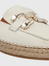 Sandalia tipo mule con base de yute estilo alpargata, confeccionada en cuero color blanco. Presenta una puntera redonda y un detalle decorativo metálico en tono dorado sobre el empeine.
