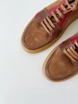Zapatillas acordonadas de cuero marrón con detalles en rojo y suela de goma color caramelo.