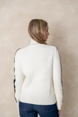 Buzo de punto acanalado color beige, con cuello alto, corte oversize y mangas largas. Presenta costuras decorativas en color negro que recorren los hombros y las mangas.