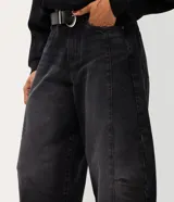 Pantalón baggy balloon de jean negro, tiro medio, con calce amplio, recortes estructurales y botamanga ajustada. Incluye bolsillos delanteros y traseros, y un cinturón de PU negro con hebilla metálica circular.