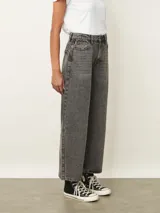 Jean de corte wide leg en color gris con efecto lavado. Presenta tiro medio, cierre frontal con botón y bolsillos laterales y traseros.