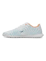 Championes de fútbol Under Armour Shadow Club 4 Turf, diseñados para césped artificial. Presentan un diseño en color blanco con detalles gráficos en azul y toques en naranja. Cuentan con empeine sintético, cordones centrales y suela de goma con tacos multidireccionales para un agarre óptimo.