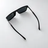 Lentes de sol polarizados con armazón negro mate, formato rectangular envolvente y patillas combinadas en metal gris oscuro y negro.