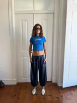Pantalón de corte holgado y estilo relajado, confeccionado en tela satinada color azul oscuro. Presenta cintura elástica con cordón ajustable, bolsillos laterales y terminación en los tobillos con elástico, logrando un efecto abullonado.