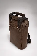 Matera mochila unisex de cuero marrón, con diseño estructurado, bolsillo frontal con cierre, asas superiores y correas ajustables.