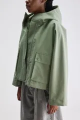 Campera de calce relajado y silueta amplia color verde, con capucha integrada, cierre frontal con cremallera oculta por cartera de broches y bolsillos delanteros con solapa.