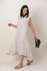 Vestido midi de lino color beige, sin mangas y con cuello redondo. Cuenta con un diseño irregular con detalle de volado vertical a un costado.
