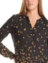 Blusa de gasa con estampado abstracto en tonos amarillos sobre fondo negro. Presenta cuello mao con escote en V y cierre frontal parcial con botones. Las mangas son largas y cuentan con presillas para ajustar su largo.