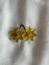 Aros tipo argolla dorada con dije colgante en forma de estrella de acrílico color rosa.