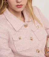 Campera corta de tweed color rosa, con cuello camisero, bolsillos delanteros con solapa y botones dorados estilo escudo.