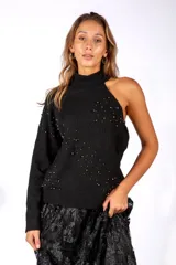 Sweater de punto negro con diseño asimétrico de un solo hombro y cuello alto. Presenta un patrón de rombos en relieve y está decorado con pequeñas tachas metálicas distribuidas por toda la prenda.