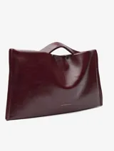 Bolso tipo clutch de Adolfo Dominguez en color bordó con acabado brillante y textura craquelada. Cuenta con un compartimento principal con cierre magnético, bolsillo interior con cremallera, asa de mano integrada y asa larga regulable y extraíble.