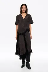 Vestido midi de corte línea A, color negro con efecto lavado, escote en pico y manga corta. Presenta detalles de encaje negro aplicado de forma asimétrica en el lateral y el bajo irregular.