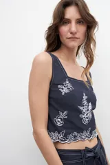 Top azul marino con breteles finos y escote cuadrado. Presenta bordados florales blancos en el frente y en el ruedo.