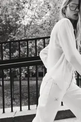 Pantalón de jean blanco, tiro superalto, con piernas amplias y corte holgado. Presenta tachas decorativas en forma de estrella o copo de nieve distribuidas por toda la prenda.