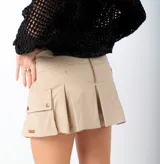 Short pollera beige de estilo cargo, con bolsillos laterales con solapa y broches, y detalle de tablones en la parte trasera.