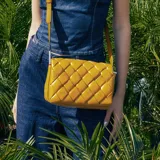 Bandolera color habano con diseño entrelazado, correa regulable, acceso con botón magnético y solapa, herrajes plateados y bolsillo interno con cierre.